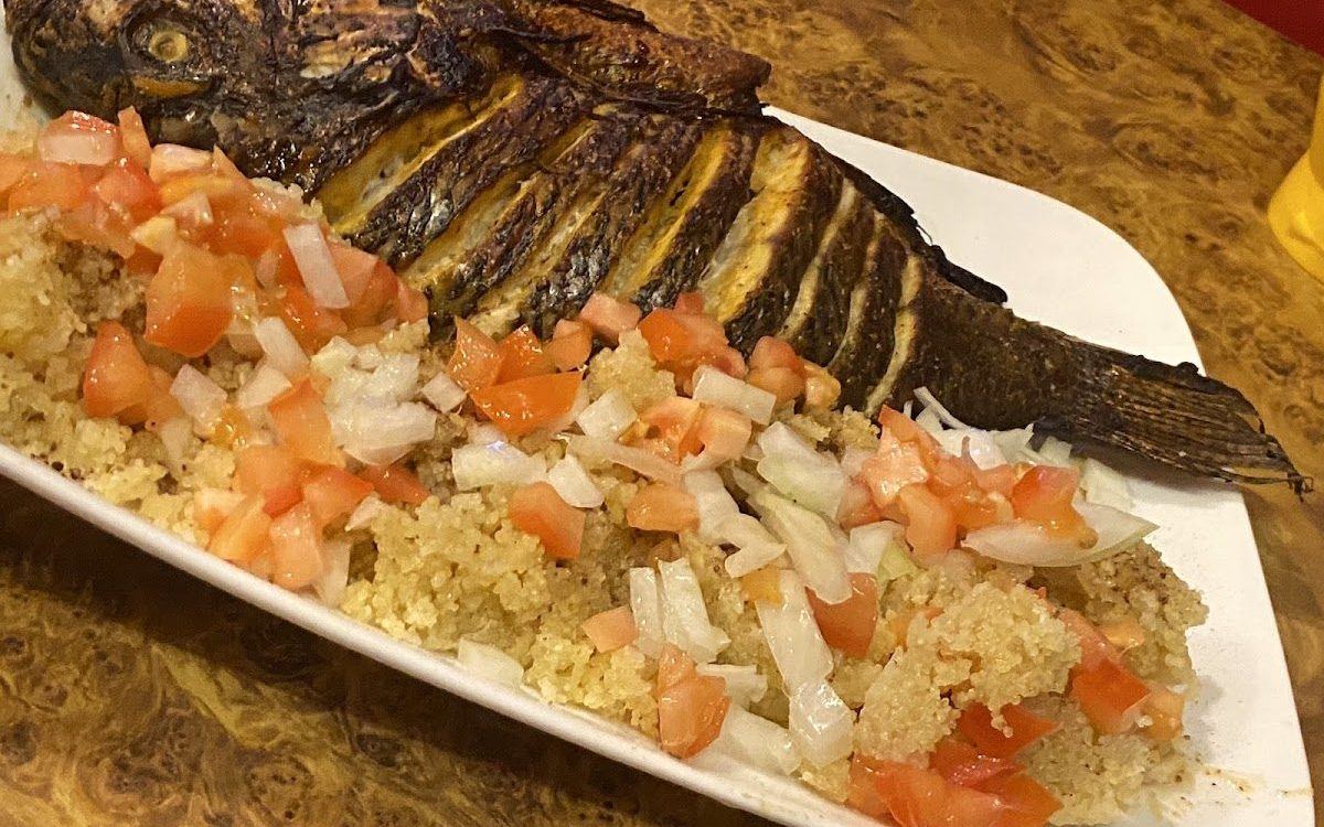 Poisson braisé entier servi avec de l'attiéké, des tomates et des oignons frais